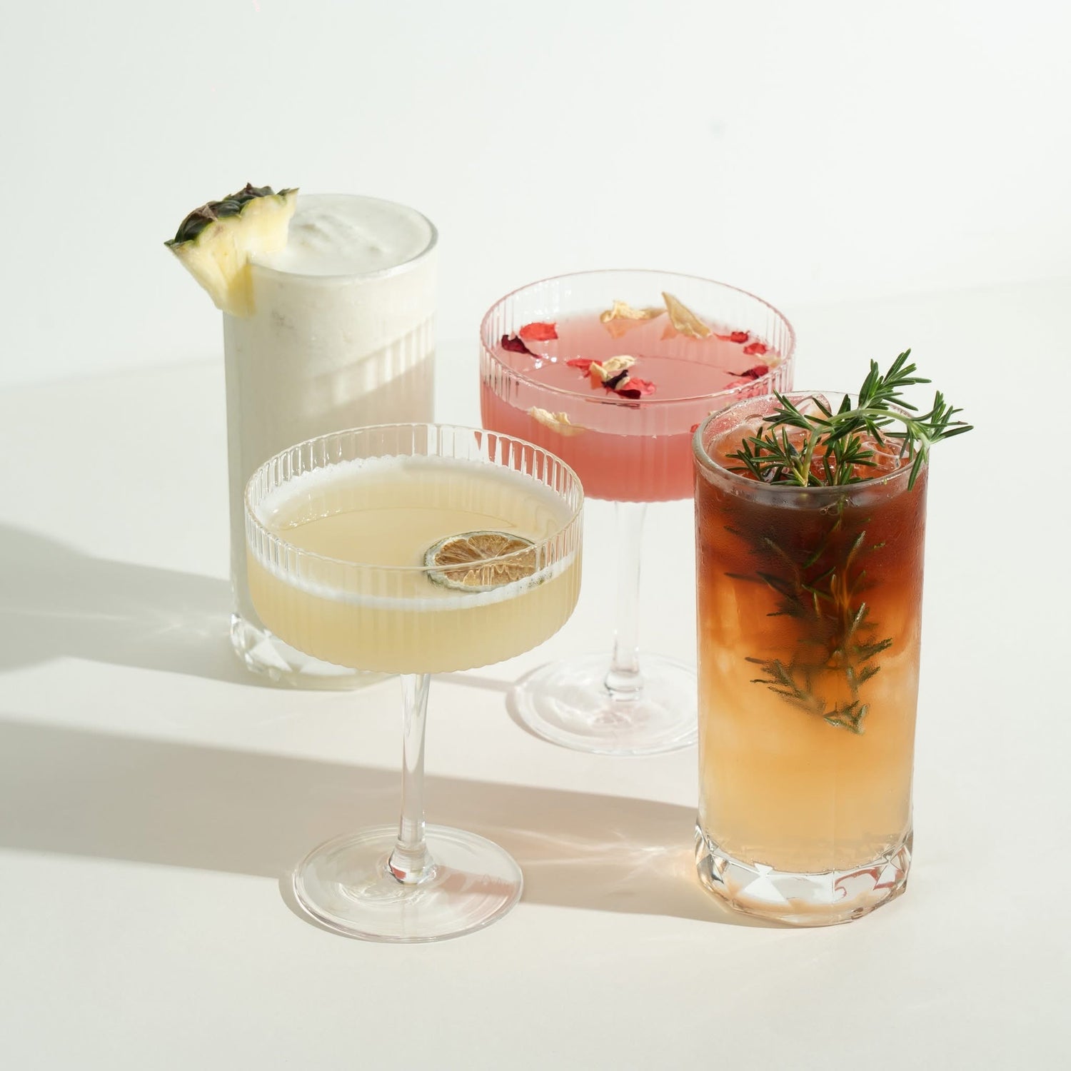 Four cocktails in different glasses with garnishes on a white background